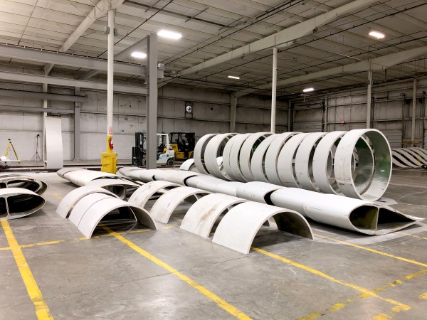 Curved white pieces of old wind turbines sit in a large warehouse.